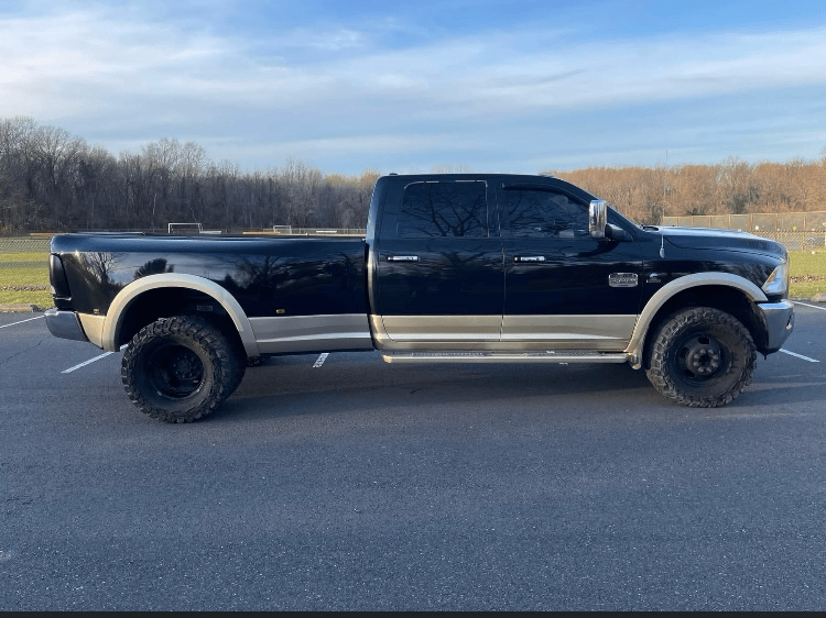 Black Rinse Rider Ram dually pickup truck with tan two-tone trim, parked in a lot under a blue sky.